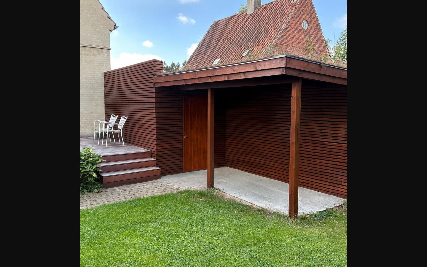 Carport i mørkt træ med tilstødende terrasse og facadebeklædning