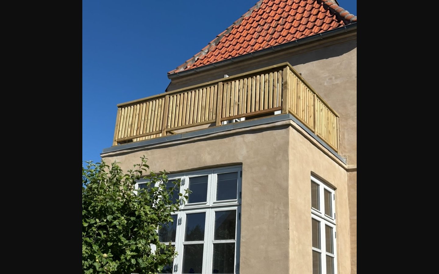Tagterrasse med trærækværk set udefra på pudset facade